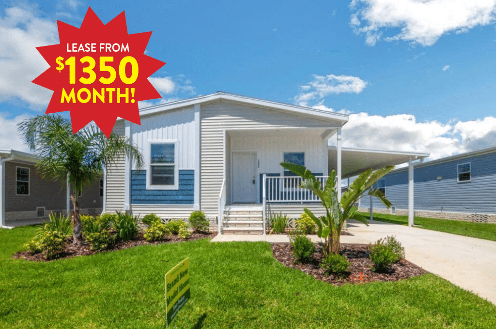 Single-story white manufactured home with porch, surrounded by a green lawn and palm trees, with a sign stating “Lease from $1350 month!” in the top left corner.