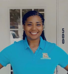 Smiling woman in a blue polo shirt standing in front of a door with the number 500.