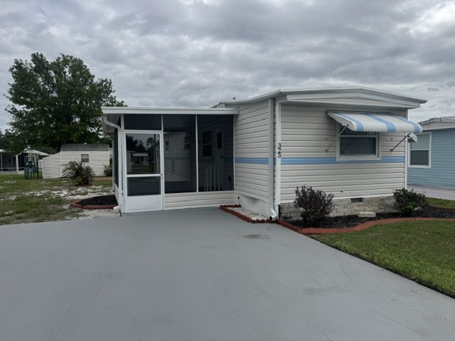 White mobile home with blue accents, screened porch, awning, and paved driveway under a cloudy sky.